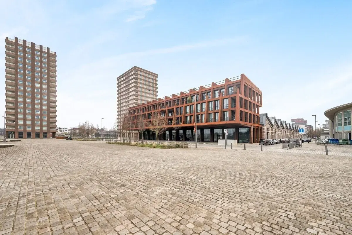 Modern apartment building with a rust-coloured steel facade on a paved square in Antwerp