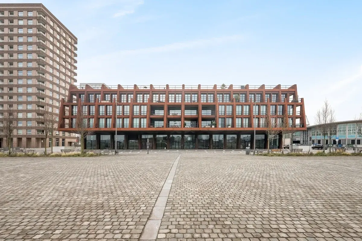 Modern apartment building with a rust-coloured steel facade on a paved square in Antwerp